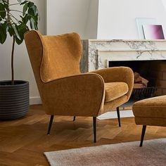 an orange chair and footstool sitting in front of a fireplace with a potted plant