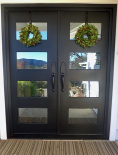 two christmas wreaths on the front doors of a house with glass and wood panels