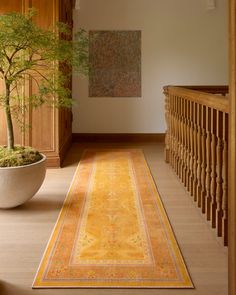 a long yellow rug is on the floor in front of a plant and staircase railing