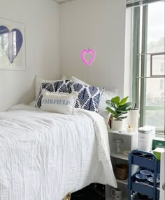 a white bed sitting next to a window in a bedroom under a pink heart hanging on the wall