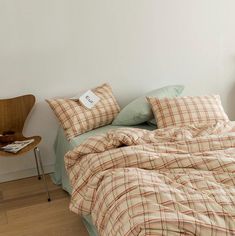 an unmade bed with plaid sheets and pillows on the floor next to a chair