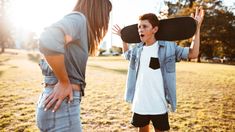 a woman holding a skateboard over her head while standing next to a young boy