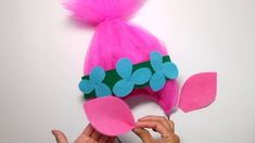 a person holding up a pink and blue hat with flowers on the top of it