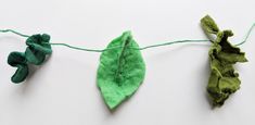 three green leaves are hanging from a string on a white surface, and one leaf is still attached to the string