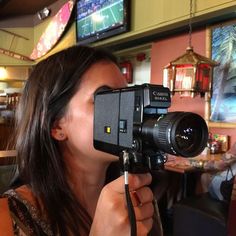 a woman holding a camera up to her face while sitting at a table in a restaurant