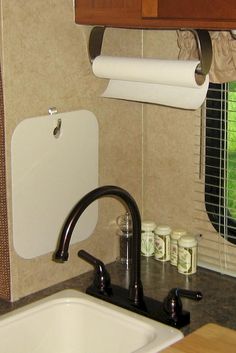 a kitchen sink under a window next to a toilet paper roll