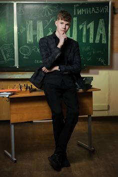 a young man sitting at a desk in front of a blackboard