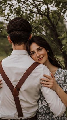 a man and woman embracing each other in front of some trees with their backs to the camera