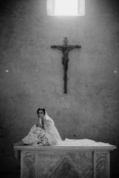 a woman sitting on top of a white table in front of a cross