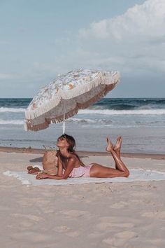 a woman laying on top of a sandy beach next to the ocean under an umbrella