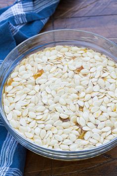 a glass bowl filled with sunflower seeds on top of a wooden table next to a blue and white towel