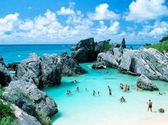 many people are swimming in the water near some rocks and boulders at an ocean beach