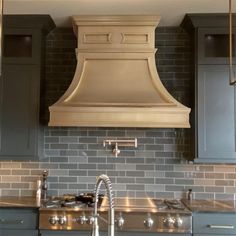 a kitchen with gray cabinets and a large hood over the stove in front of it