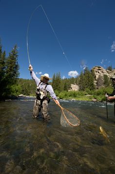 a man standing in the water while holding a fishing rod and a fish on it