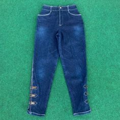 a pair of blue jeans with gold buttons on the side, laying on green carpet