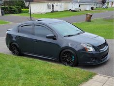 a black car parked on the side of a road next to a grass covered yard