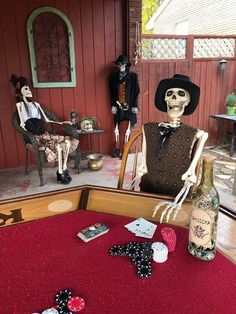 two skeletons sitting on chairs in front of a table with playing cards and wine bottles