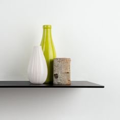 two vases sitting on top of a shelf next to a tree stump in front of a white wall