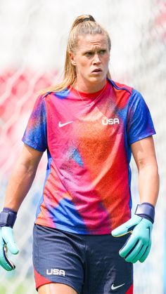 a female soccer player wearing blue gloves and a tie dye t - shirt with the usa on it