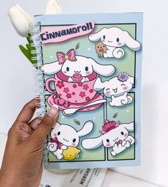 a hand holding up a notebook with an image of bunnies and teacups on it