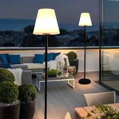 two lamps on top of a wooden deck next to couches and tables with plants