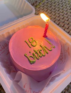 a pink birthday cake with a lit candle on it's top in a plastic container