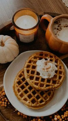 three waffles on a plate with syrup and pumpkins around them, along with two cups of coffee