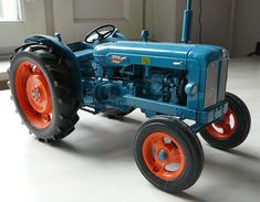 an old blue tractor with orange wheels on a white floor in front of a window