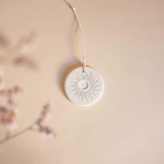 a white ceramic ornament hanging from a tree branch with flowers in the background