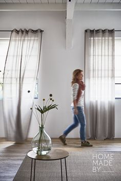 a woman walking through a living room next to a vase filled with flowers