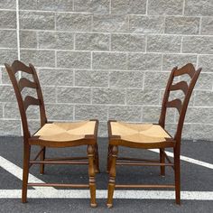 two wooden chairs sitting next to each other in front of a brick wall and parking lot