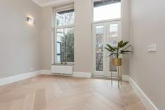 an empty room with wood flooring and two large windows in the corner, along with a potted plant