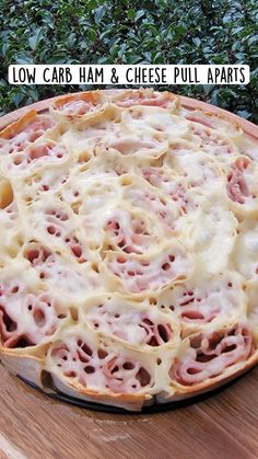 a pizza sitting on top of a wooden table covered in cheese and ham toppings