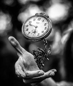 black and white photograph of a person holding an old clock in their hand with the time being 11 00