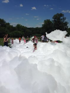 many people are playing in an enormous pile of white foam at the park on a sunny day