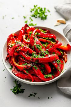 a white bowl filled with red peppers and parsley on top of a gray napkin