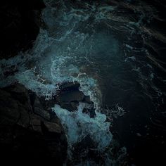 the water is dark and choppy as it looks like waves are crashing against the rocks