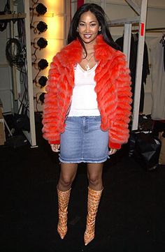 a woman standing in front of a rack with clothes on it's sides and wearing an orange fur coat over her shoulders