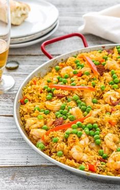 a large pan filled with rice and shrimp next to two glasses of beer on a table