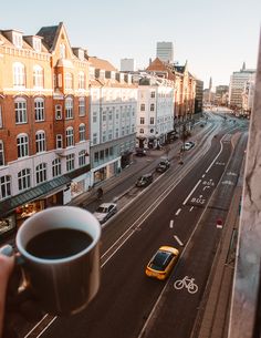 a cup of coffee is held up in front of a city street with cars and buildings