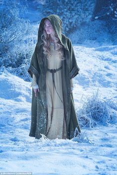 a woman in a hooded robe walking through the snow