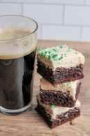 three brownies with green frosting next to a cup of coffee on a wooden table