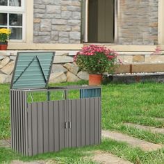 a metal trash can sitting in the middle of some grass next to a house and flowers