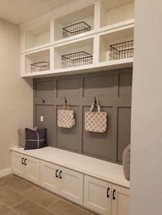 a mud room with white cabinets and baskets on the wall, two bags hanging from hooks