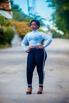 a woman standing on the side of a road wearing leggings and high heels