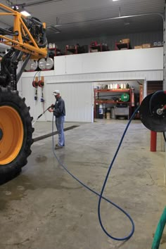 a man is using a hose to clean the floor in a garage with a tractor