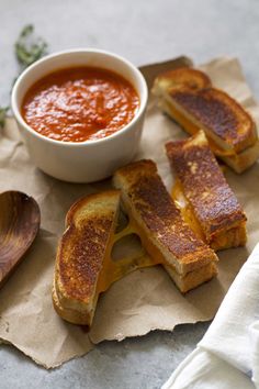 grilled cheese sandwiches on parchment paper with a bowl of tomato soup in the background