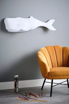 an orange chair sitting in front of a white fish sculpture on the wall next to a can of soda