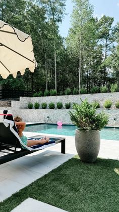 a woman laying in a chaise lounge next to a swimming pool with an umbrella over it