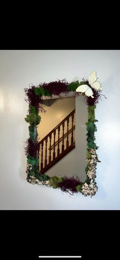 a mirror that is on the wall with grass and flowers around it, reflecting an image of a stair case